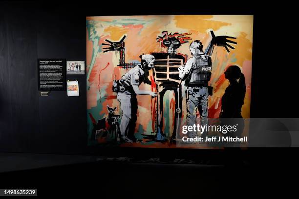 Matilda Lask stands next to 'Basquiat being stop and searched' on display at the new show by artist Banksy 'Cut & Run' which opens on the 18th at...