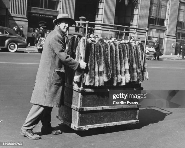 Man pushing a wheeled clothes rail of fur coats along a road in New York City, New York, circa 1945.