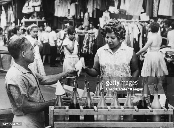 Woman with her hair in curlers buying a cone of shaved ice from a street vendor in the Harlem neighbourhood of Upper Manhattan, New York City, New...