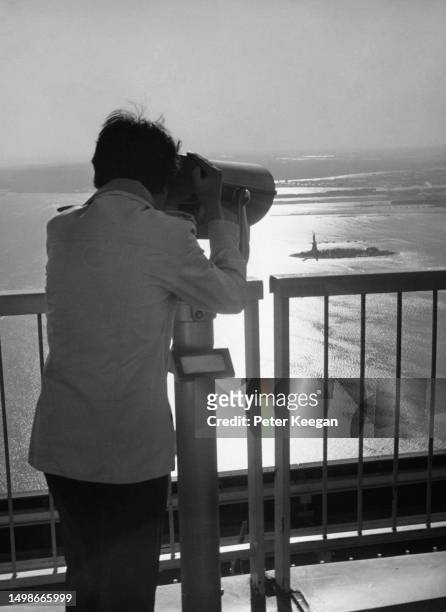 Man using a tower viewer to look at the Statue of Liberty on Liberty Island in New York Harbor, from the observation deck of the World Trade Center...