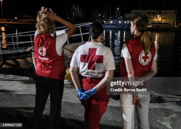 Members of the Red Cross wait outside of a hangar where more than 100 migrants have been temporarily housed as the Greek Coast Guard ship with 79...