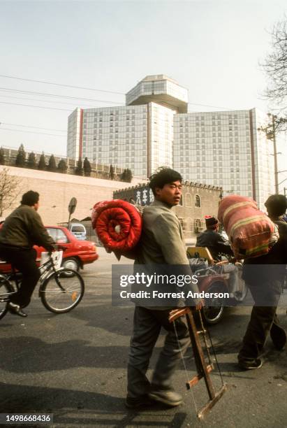 View of pedestrians carrying bedrolls and cyclists on a street near the Great Wall Sheraton Hotel, Beijing, China, 1990s.