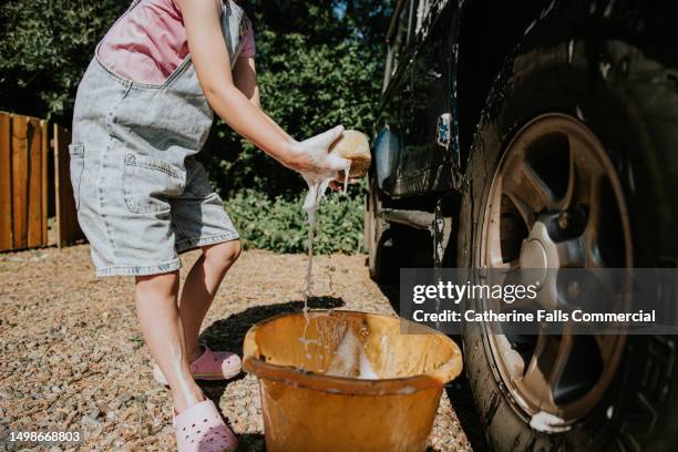 a child uses a bucket and sponge to wash a large 4x4 blue car on a sunny day - hubcap stock pictures, royalty-free photos & images