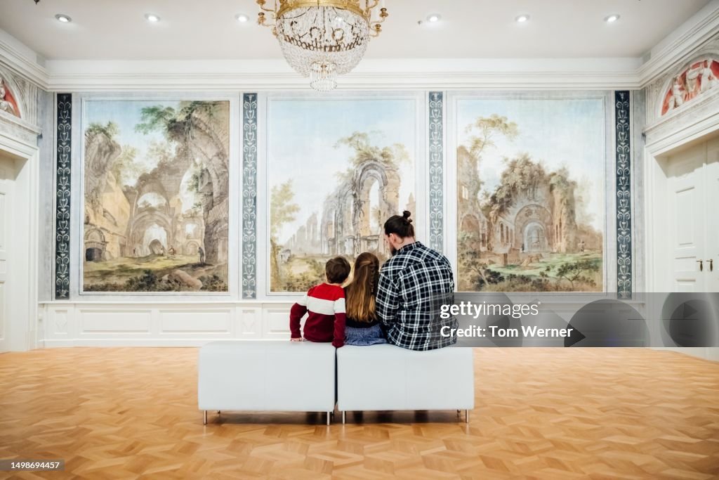 Father Enjoying Paintings On Display While Visiting Museum With Children