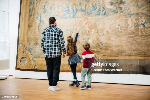 young girl pointing up towards large painting while exploring museum with family - family museum stock pictures, royalty-free photos & images