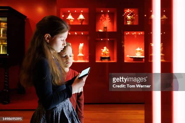 brother and sister looking at smartphone while exploring museum exhibit - boy skirt stock pictures, royalty-free photos & images