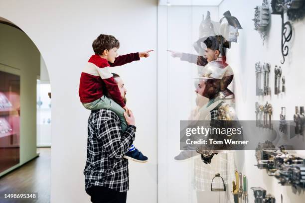 young boy sitting on father's shoulders while visiting museum - family museum stock pictures, royalty-free photos & images