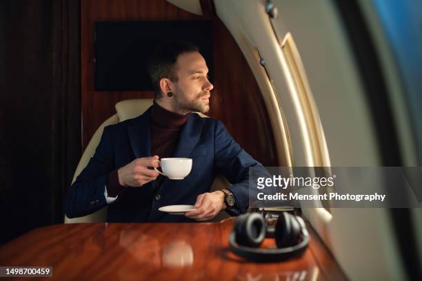 confident ceo businessman enjoys his cup of coffee in first class on a private plane - first class plane stock-fotos und bilder