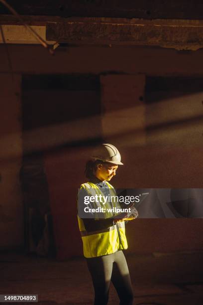 female worker indoors on construction site with sun beam falling on dust with ppe on tablet - engenheiro civil imagens e fotografias de stock