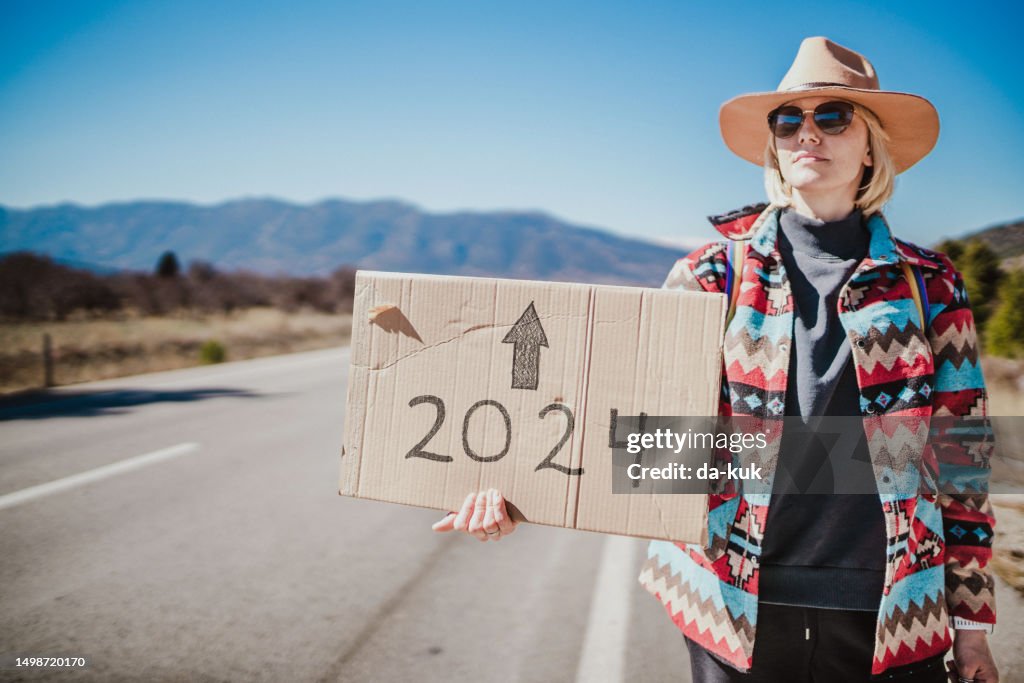 Bis 2024. Frau trampt allein und hält ein Pappschild in der Hand