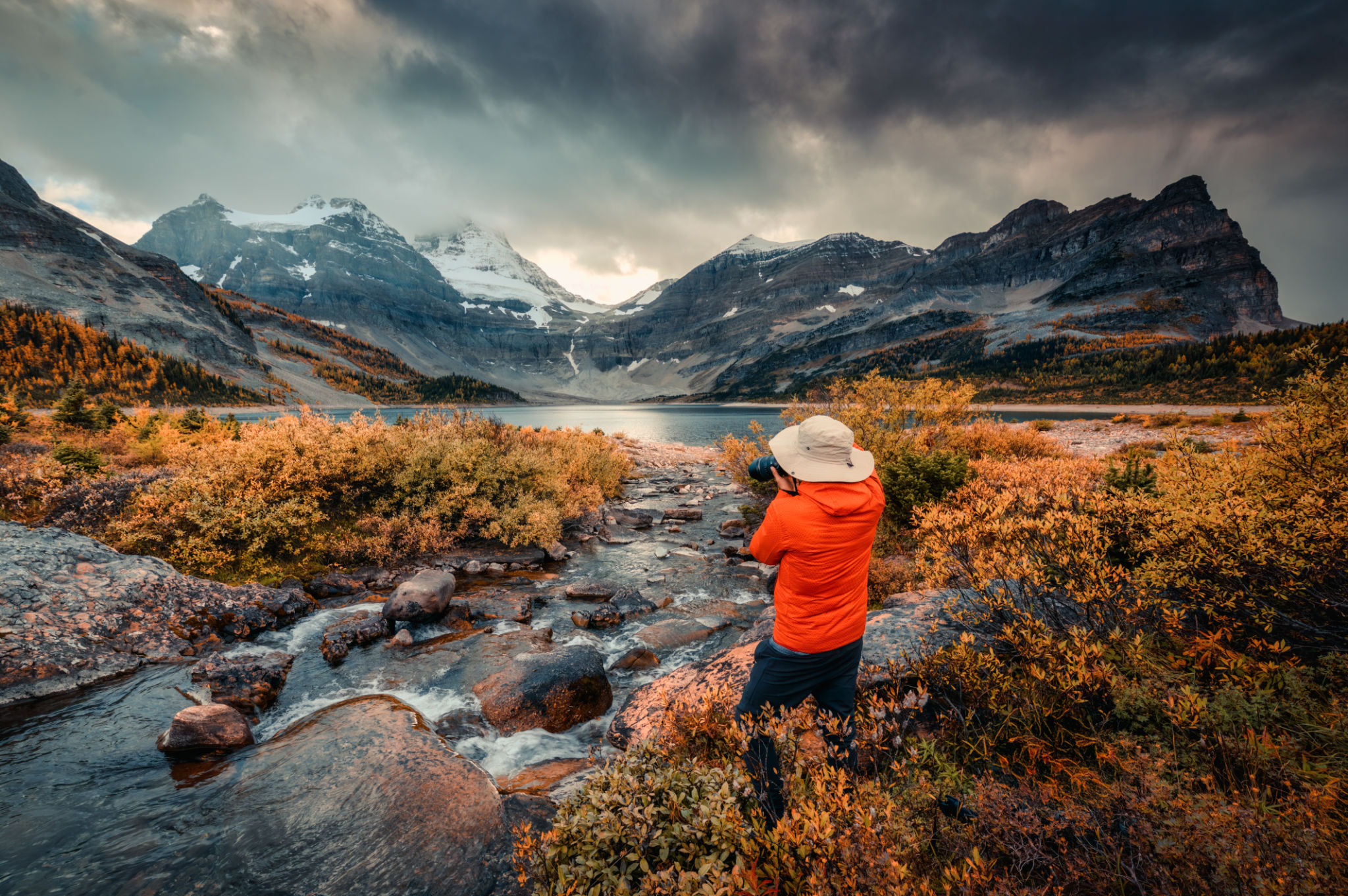 Travel photographer man taking a photo with camera at mount assiniboine in autumn wilderness by lake magog on moody day Travel photographer man taking a photo with camera at mount assiniboine in autumn wilderness by lake magog on moody day