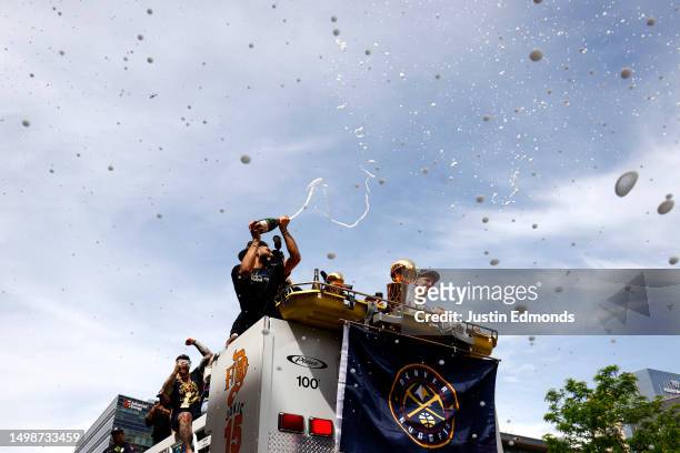 Jamal Murray sprays champagne with Nikola Jokic and the Larry O'Brien Championship Trophy during the Denver Nuggets victory parade and rally after...