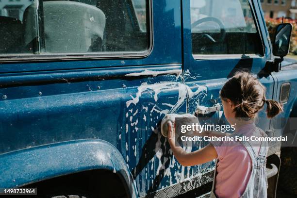 a child uses a yellow sponge to wash a large blue 4x4 car - hubcap stock pictures, royalty-free photos & images