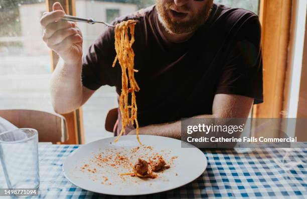 a man eats a plate of spaghetti bolognese with meatballs at a  dining table - pasta geniessen stock-fotos und bilder