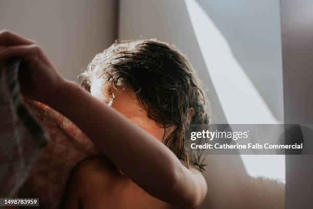 a independent young child gets herself ready, drying her wet hair. - envuelto en una toalla fotografías e imágenes de stock