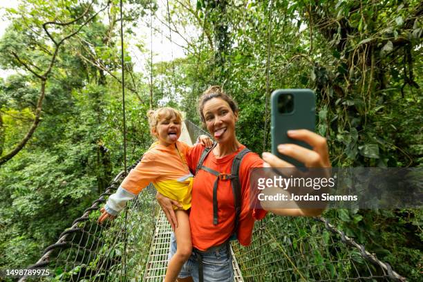a mother and her daughter taking a selfie on a bridge in the rainforest of costa rica - la fortuna stock pictures, royalty-free photos & images