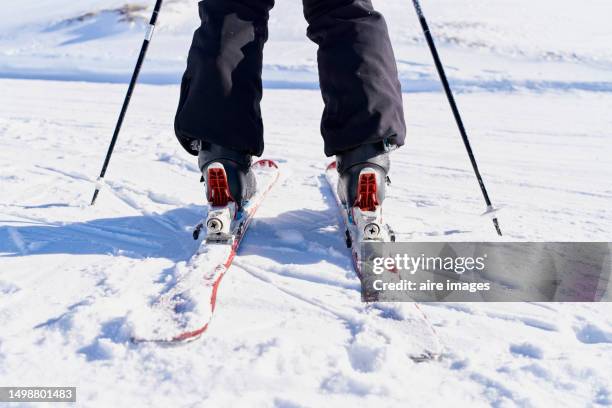 rear view of an unrecognizable person on a snowy mountain wearing warm black pants, skis and ski poles - ski pants fotografías e imágenes de stock