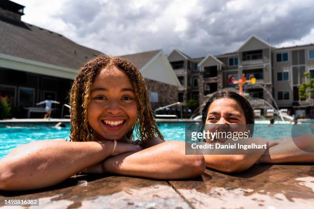 two girls, around 13 to 15 years old, enjoy the poolside oasis on a sunny summer day. with one girl's curly blond-dyed hair and the other's cascading dark locks, their smiles and laughter create an atmosphere of pure delight. - 12 13 14 15 years girl stock pictures, royalty-free photos & images