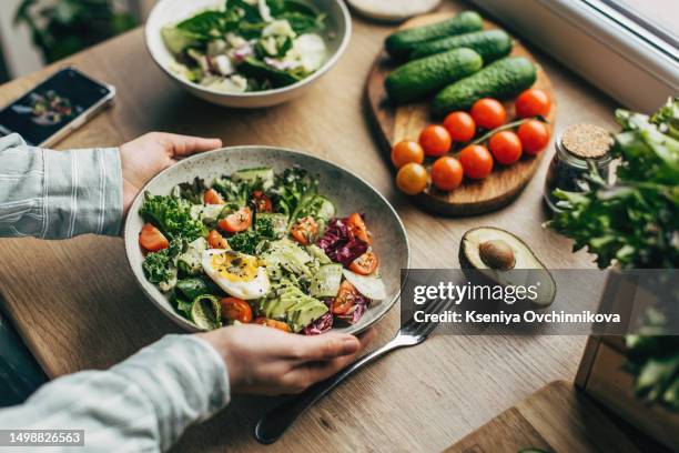 woman mixing delicious superfood salad ingredients with wooden spoons in kitchen - healthy food stock pictures, royalty-free photos & images