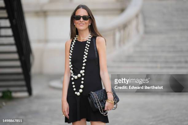 Alba Garavito Torre wears black sunglasses from Ray Ban, white pearl and gold long chain pendant earrings, a white and gold bi material pearls...