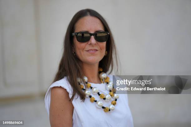 Alba Garavito Torre wears black sunglasses from Ray Ban, gold earrings, a white large pearls / gold pearls / black cordon triple necklace, a white...