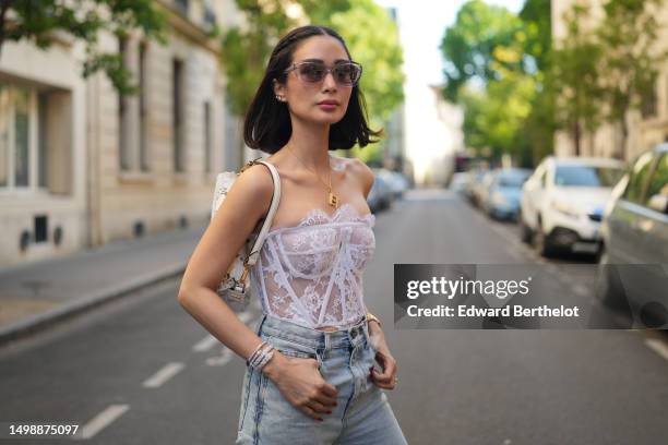 Heart Evangelista wears pale gray transparent sunglasses, diamonds earrings, a gold H large pendant necklace, a white lace print pattern shoulder-off...