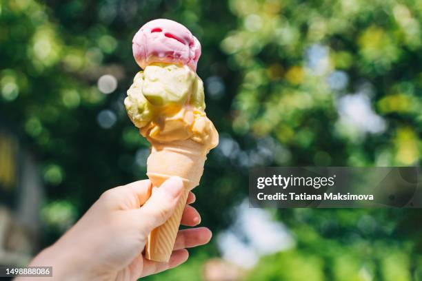 ice cream consisting of three balls in a waffle cone in a hand close-up. - kegel stock-fotos und bilder