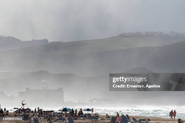people in silhouette sunbathing on the beach on a day with lots of sea spray - las palmas de gran canaria stock pictures, royalty-free photos & images