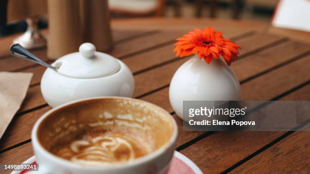 large half full cup of cappuccino coffee at the wooden table in small local cafe - gerbera daisy ストックフォトと画像