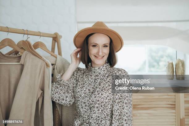 smiling young woman in wide brim hat near wooden floor hanger. - blouse stock pictures, royalty-free photos & images
