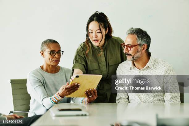 medium shot colleagues looking at data on digital tablet during meeting - mh stock pictures, royalty-free photos & images