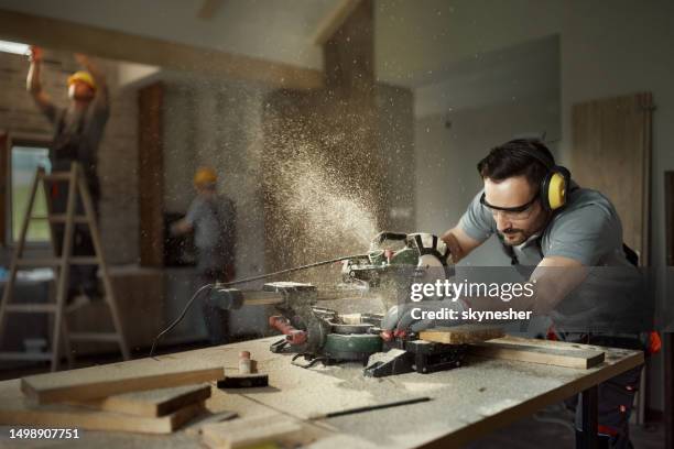 male carpenter cutting wood plank with electric saw at construction site. - carpentry tools stockfoto's en -beelden