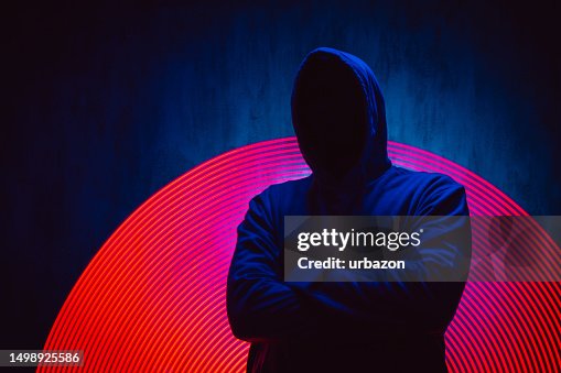 Aterrador hombre sin rostro con una sudadera con capucha bajo luces de neón Aterrador hombre sin rostro con una sudadera con capucha bajo luces de neón