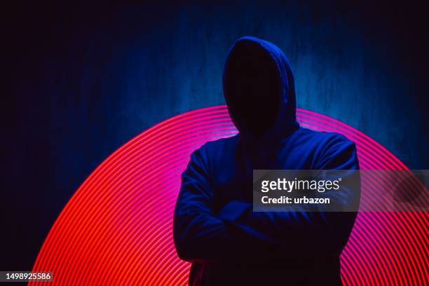 homem sem rosto assustador em um capuz sob luzes de néon - ladrão - fotografias e filmes do acervo