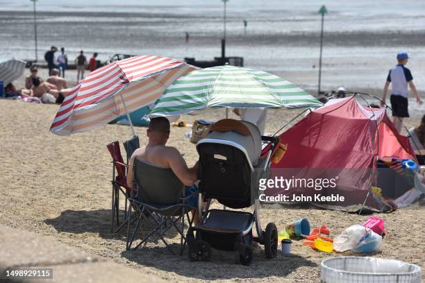 Parent sits by a baby in a pram under a parasol during the warm sunny weather on Jubilee beach on June 10, 2023 in Southend, England. Heat health...
