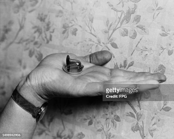 Very small loudspeaker, placed on a coin in the palm of a hand to give a sense of scale, United States, circa 1935.