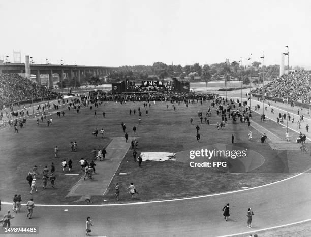 High-angle view showing festivalgoers crossing the playing field toward the stage hosting the 'Carnival of Swing', a banner above the stage bears the...