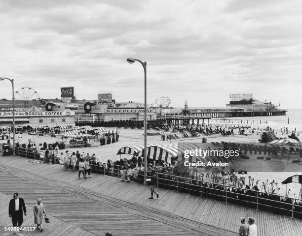 Holidaymakers on the boardwalk and beach, with the Steeplechase Pier and Steel Pier extending beyond, on the Atlantic City seafront, New Jersey,...