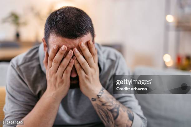 gestresster mann, der allein sitzt und sein gesicht mit beiden händen bedeckt - regret stock-fotos und bilder
