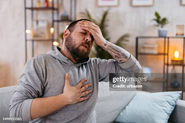 man suffering from pain sitting in the living room - breathing problems stock pictures, royalty-free photos & images