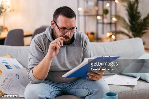 young man checking his finances at home - regular man stock pictures, royalty-free photos & images