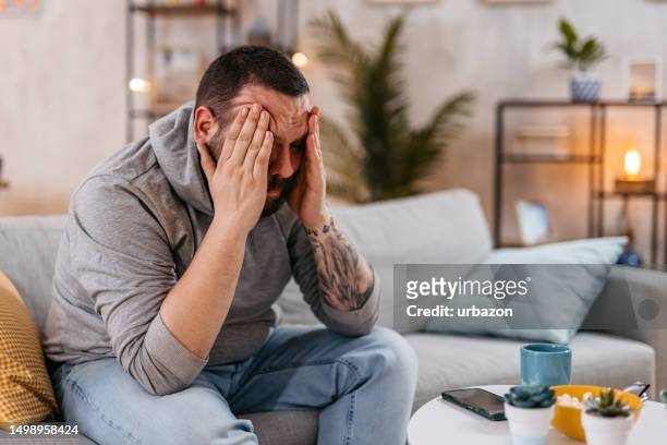 man sitting at home feeling headache and distress - hand on head stockfoto's en -beelden