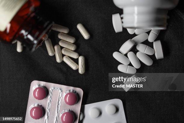 top view of pills and capsules spilling on black background with studio lightning - ibuprofen stock pictures, royalty-free photos & images