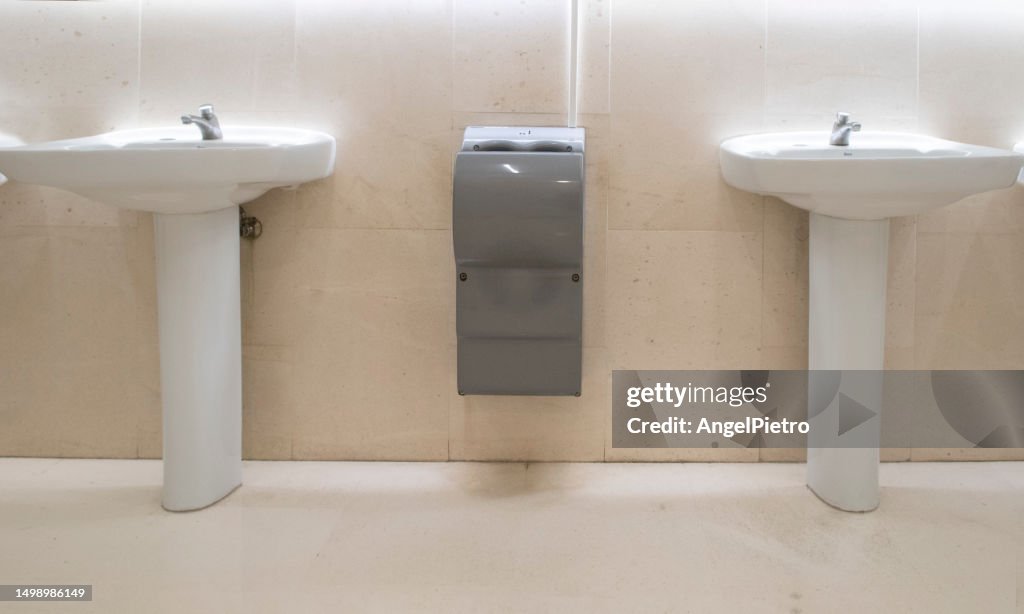 Two sinks separated by a hand-drying device in a public restroom.