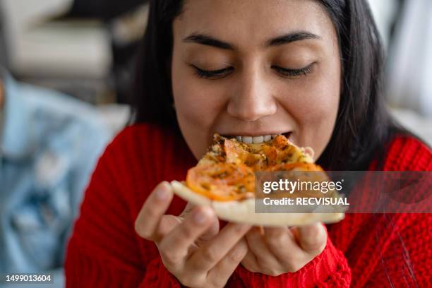 portrait of a latina woman eating pizza in her living room. - eating pizza stock pictures, royalty-free photos & images