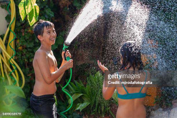 children in swimsuits playing with water from a hose - mjrodafotografia stock pictures, royalty-free photos & images