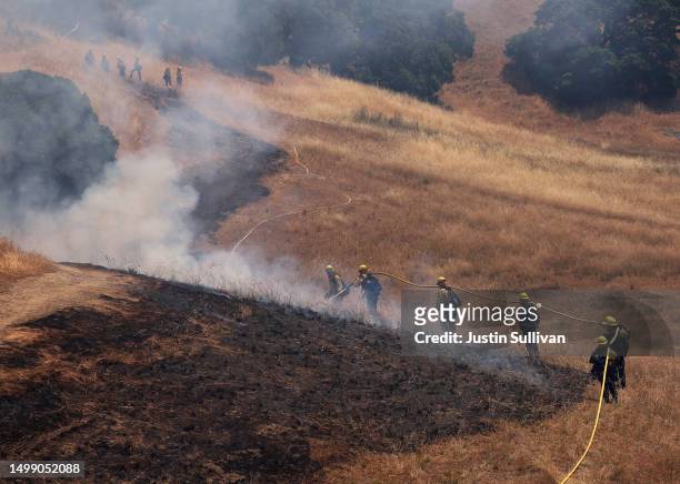 Marin County firefighters pull a hose up a hill during a controlled burn training on June 16, 2023 in San Rafael, California. Newly hired seasonal...