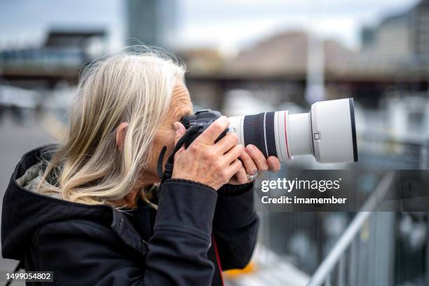 side view of senior woman taking photos with dslr camera, outdoor, background with copy space - lente telefotográfica imagens e fotografias de stock