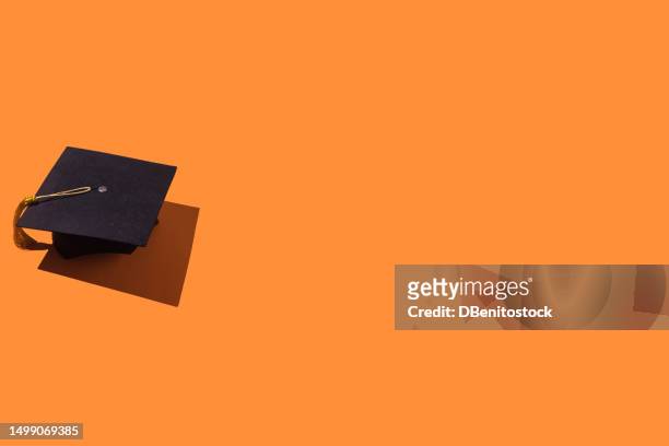 black graduation cap with gold tassel with hard shadow, on the left side, on orange background. graduation, achievement, goal, degree, master's, bachelor's, university, college and success concept. - draft first round stock pictures, royalty-free photos & images
