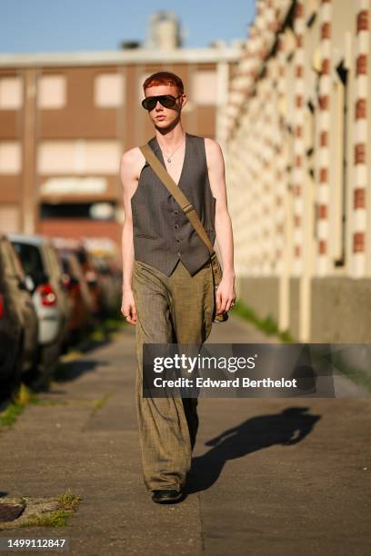 Guest wears black sunglasses, silver small earrings, a gold chain and green pendant necklace, a dark brown sleeveless / buttoned suit gilet, a brown...